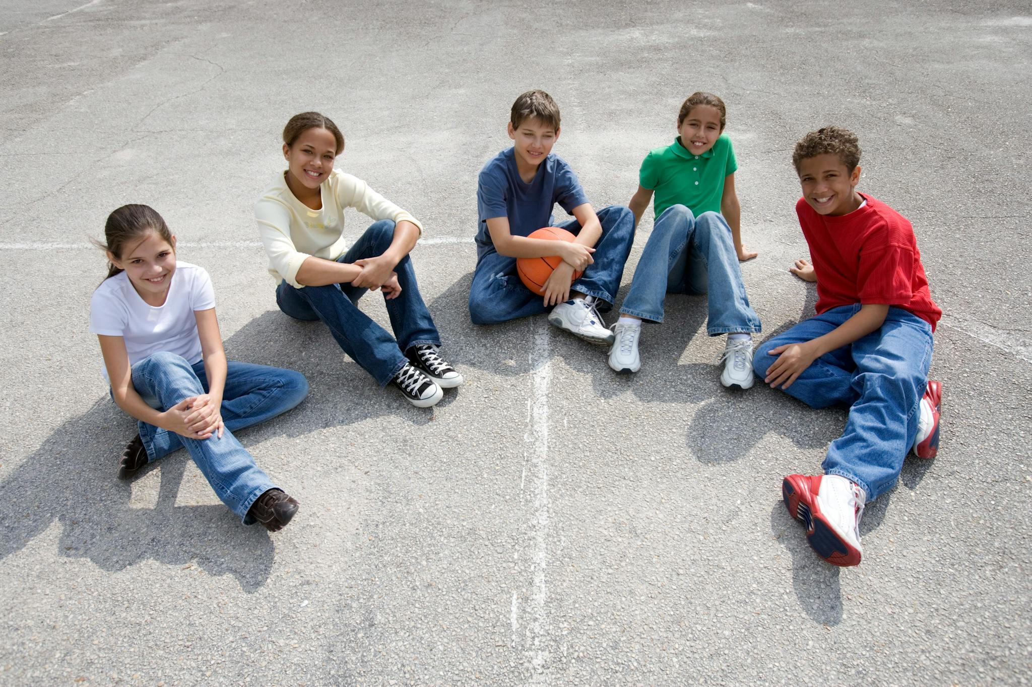 A diverse group of teenagers sitting on concrete, enjoying friendship and sports outdoors.
